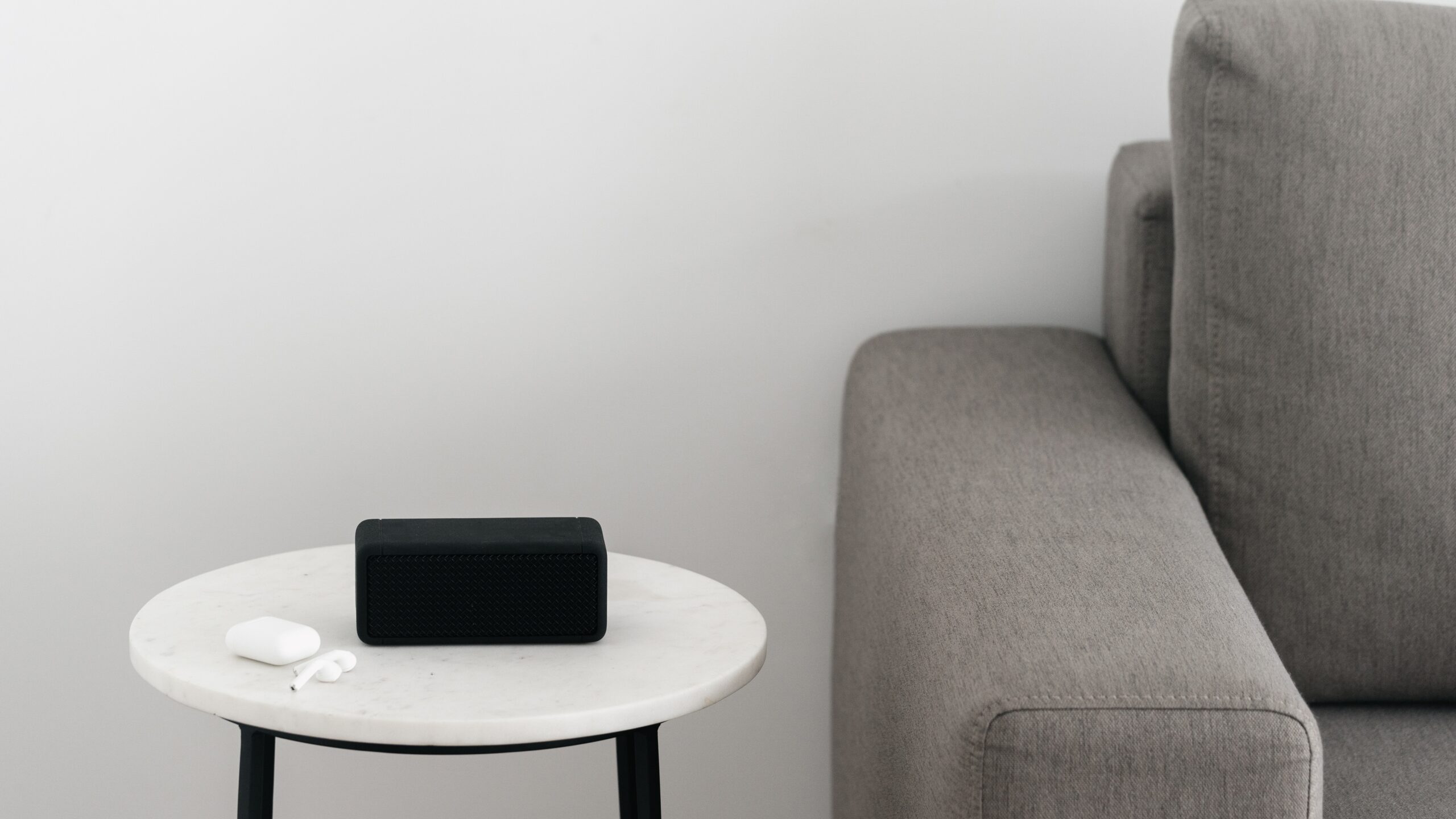 Speaker Sonos nero su un tavolino rotondo accanto a un divano grigio con auricolari wireless.